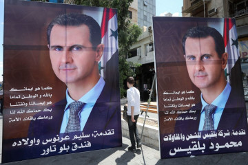 People walk next to election campaign billboards in Damascus depicting Syrian President Bashar al-Assad. [Getty]