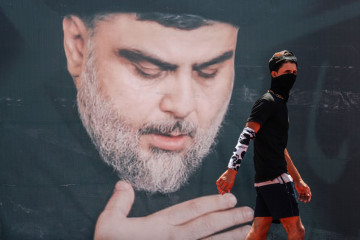 A youth walks in front of a large poster of Iraq's populist Shia cleric Moqtada Sadr, in Sadr City, east of the capital Baghdad, on 15 July 2021. [Getty] 