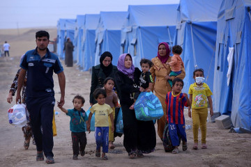 An Iraqi family walks past tents at a temporary camp set up to shelter Iraqis fleeing violence in Iraq's northern Nineveh province on June 12, 2014, in Aski kalak, 40 kms West of Arbil. [Getty]