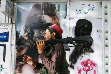 A Taliban fighter walks past a beauty salon with images of women defaced using spray paint in Shar-e-Naw in Kabul on August 18, 2021. (Photo by Wakil KOHSAR / AFP) (Photo by WAKIL KOHSAR/AFP via Getty Images)