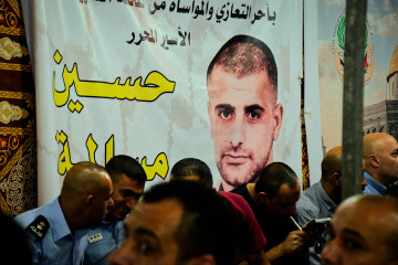 A banner with the picture of Hussein Masalmah at his family's hall yard in Bethlehem overlooks Palestinians sitting