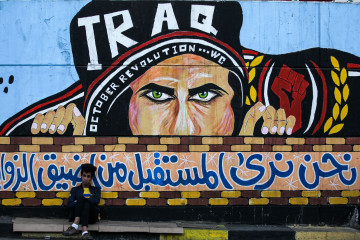 An Iraqi youth sits leaning on a wall with a graffiti mural showing a protester with text in Arabic reaing "we see the future from the narrowest angles", at the anti-government sit-in in the capital's Tahrir Square on December 24, 2019