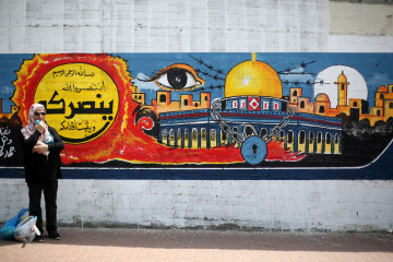 A Palestinian woman stands in front of a mural for the city of Jerusalem in Gaza City