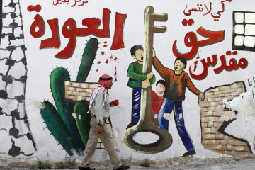 A Palestinian man walks past a mural on a wall in the West Bank city of Jenin reading in Arabic: "So that we don't forget the sacred right to return" on May 13, 2013