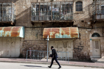 An Israeli settler walks past a Palestinian house with verandas covered in meshing with one bearing a protest sign reading in English "Arabs are prohibited, this is Apartheid St."