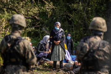 Polish border guards stand next to migrants believed to be from Afghanistan sit on the ground in the small village of Usnarz Gorny near Bialystok, northeastern Poland, located close to the border with Belarus, on August 20, 2021