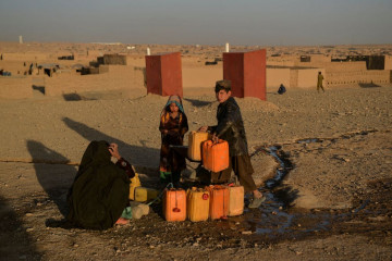 This picture taken on October 13, 2021, shows a woman and children filling tanks with water at the Shahrak Sabz Internally Displaced People (IDP) camp in Herat province. - Drought stalks the parched fields around the remote Afghan district of Bala Murghab, where climate change is proving a deadlier foe than the country's recent conflicts.