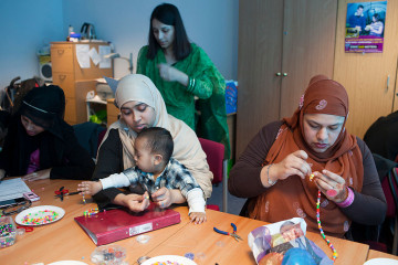 A group of Muslim mothers concentrate on threading beads during a craft workshop for parents at Marner Primary School in Tower Hamlets