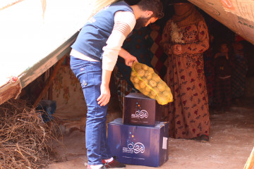 Man hands sack of potatoes to a woman in a tent