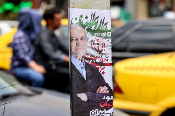 Motorists drive past an election poster for Iranian presidential candidate Masoud Pezeshkian