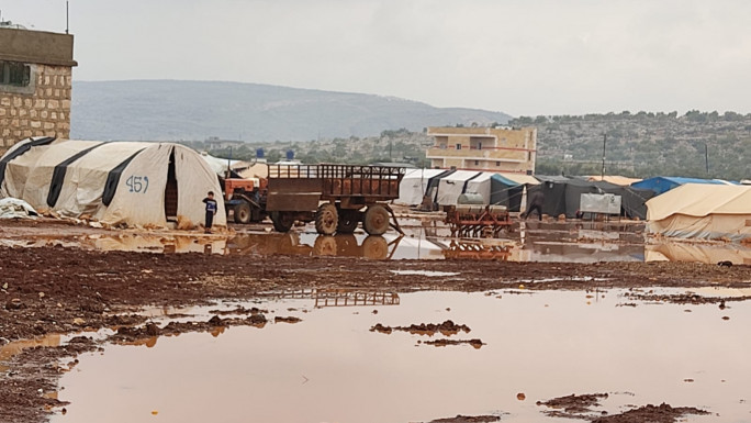 Muddy pool of water in front of a row of tents 