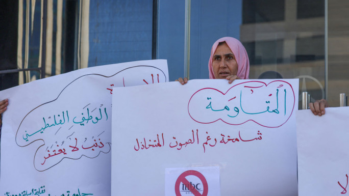 Palestinians lift placards during a rally at the entrance of a building housing the offices of Saudi broadcasters MBC, Al-Arabiya, and Al-Hadath in Ramallah in the occupied West Bank on October 21, 2024, to call for their closure [AFP/Getty]