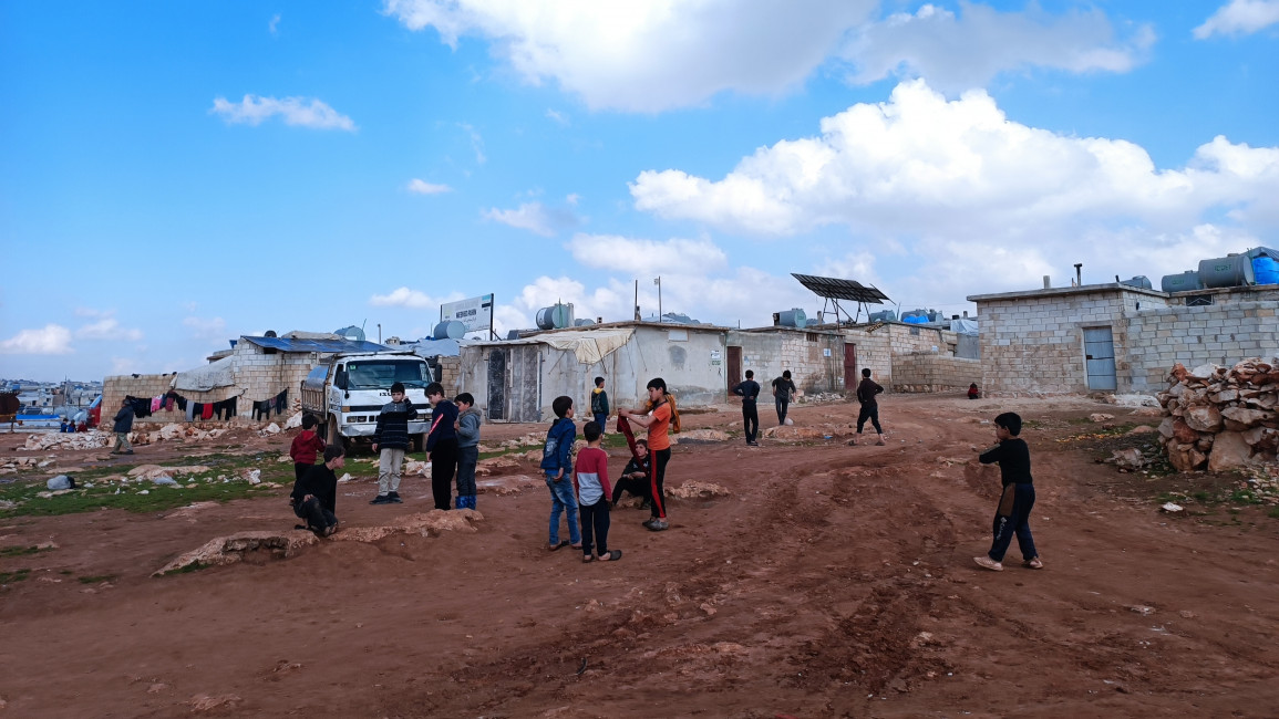 Children gathering outside in a muddy space near some buildings