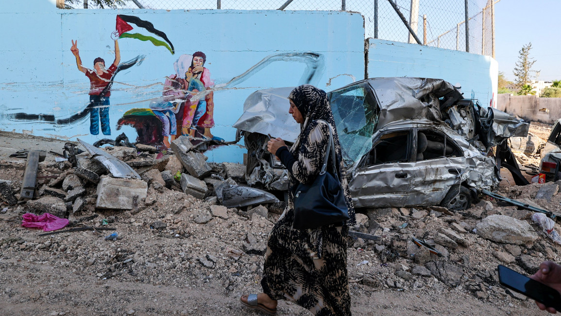 A woman walks past the wreckage of a car on a street in the occupied West Bank city of Jenin