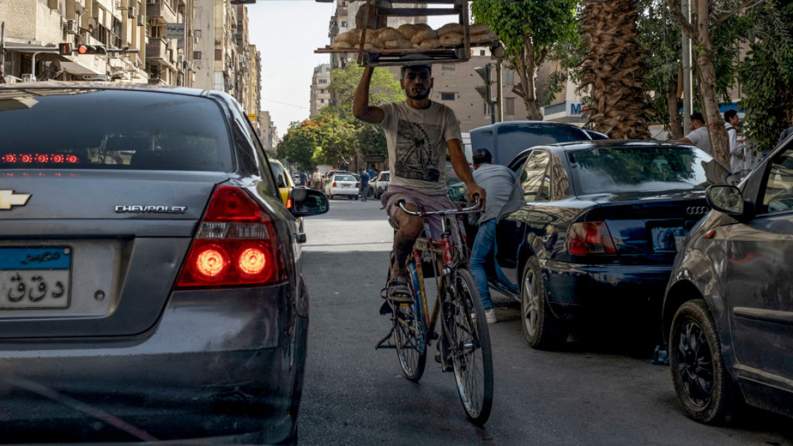 A deliveryman balances a tray of freshly baked bread while riding his bicycle through traffic in central Cairo on May 17, 2024