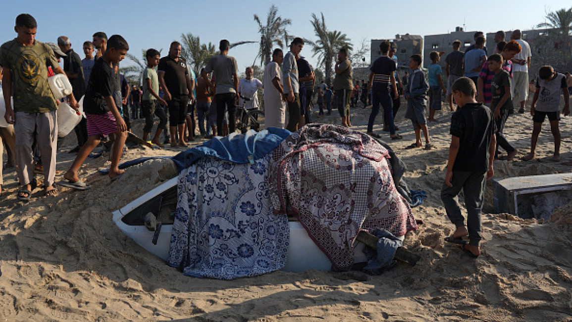 Palestinians stand next to a car covered in sand at the site of Israeli strikes on a makeshift displacement camp in Mawasi Khan Yunis in the Gaza Strip on September 10, 2024.