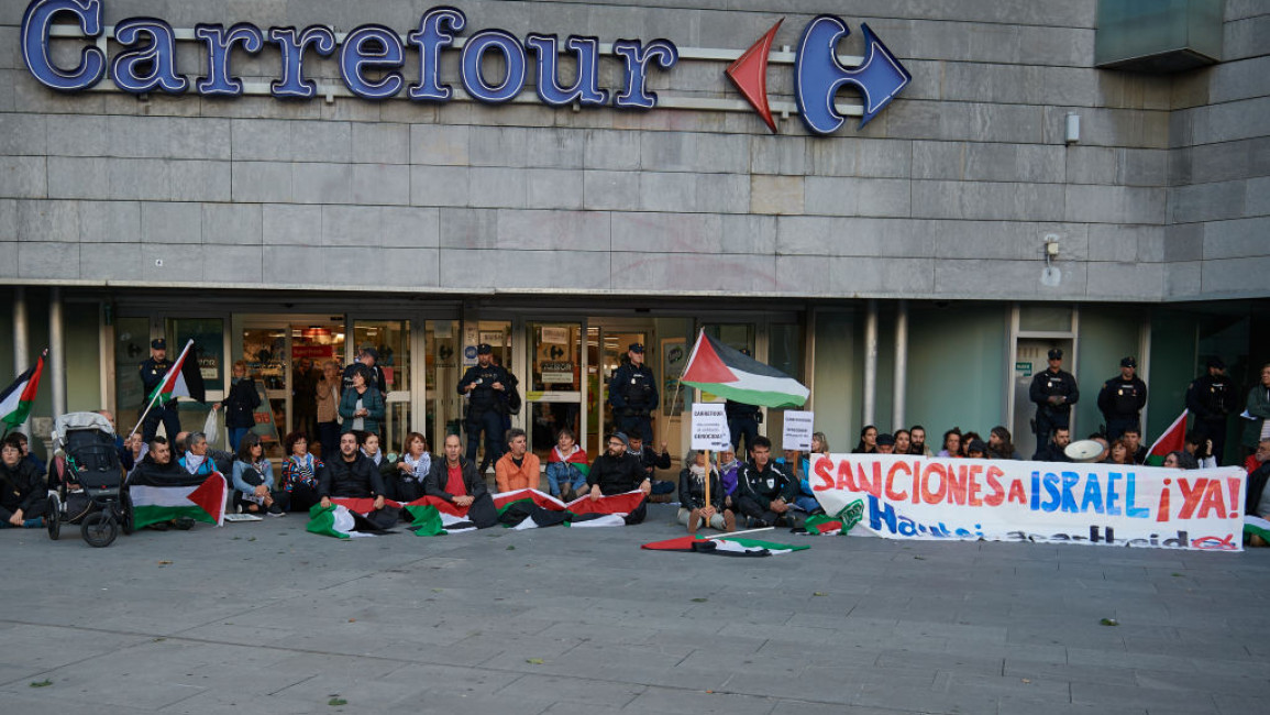 Demonstrators hold a banner and Palestinian flags outside a Carrefour store in Pamplona, Spain