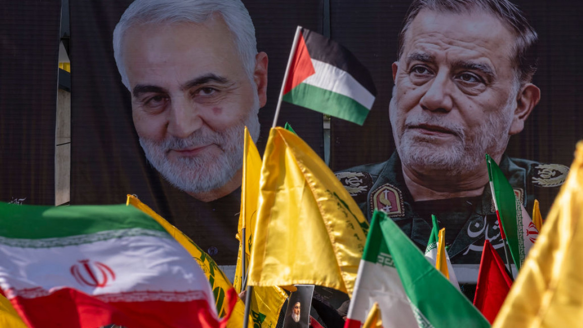 Iranian people wave a Palestinian, Iranian, and Hezbollah flags in front of portraits of IRGC Generals Qassem Soleimani and Abbas Nilforoushan, during a gathering in Tehran