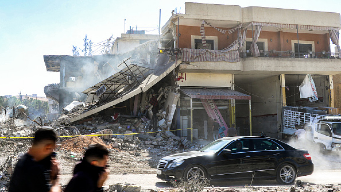 Men cover their faces as a vehicle leaves a trail of dust while moving past a destroyed building following an Israeli air strike in the village of Duris near Baalbek in Lebanon's Beqaa on October 15, 2024. (Photo by NIDAL SOLH/AFP via Getty Images)