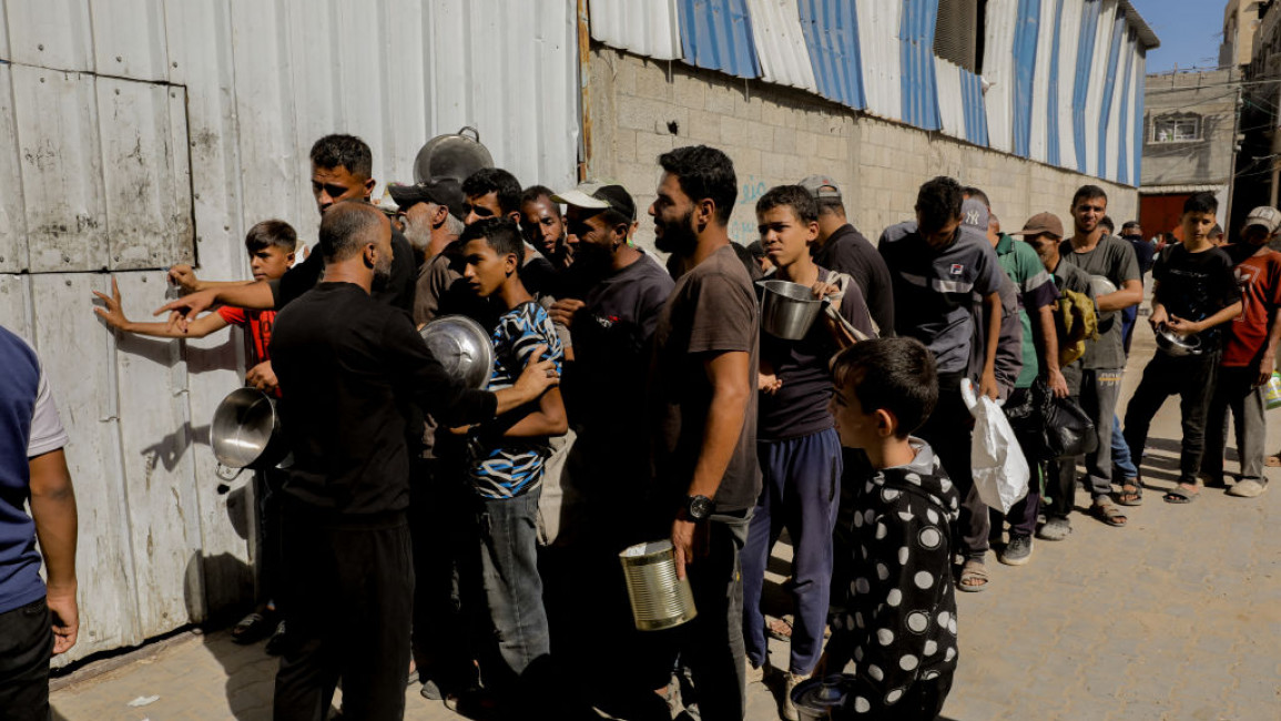 People gather with containers, waiting in long lines to receive food aid in Gaza City