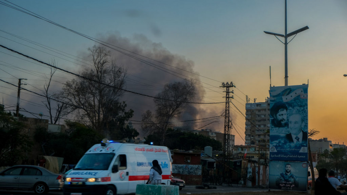 An ambulance drives past as smoke rises from buildings in Tyre, Lebanon, on 1 November 2024, following Israeli airstrikes