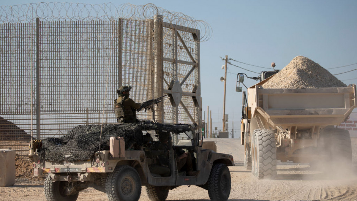 An Israeli army vehicle stands guard as a truck with gravel moves into the Gaza Strip, as seen from a position on the Israeli side of the border