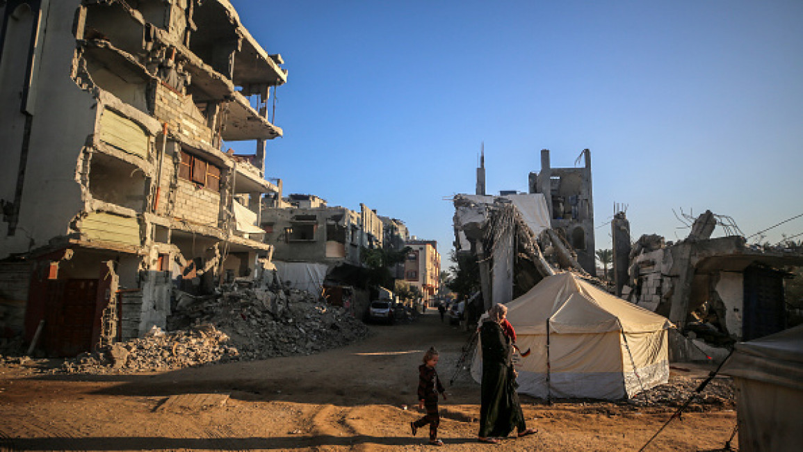 A Palestinian woman carries a child as they walk past the rubble of houses destroyed in previous strikes during the Israeli military offensive on Deir al Balah